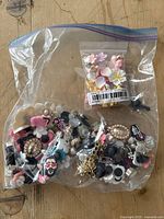Clear plastic resealable bag containing a large assortment of imitation Jibbitz shoe charms for Crocs with various flower-shaped and novelty designs