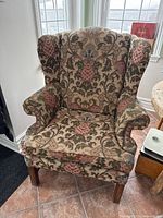 Front view of traditional wingback armchair with floral patterned fabric upholstery and wooden legs