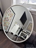Front view of the round mirror showing clear reflective glass and white rubber outside ring frame, capturing part of a room reflected in the glass.