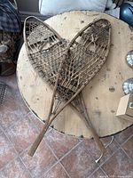 Top view of two vintage wooden snowshoes crossed over each other on a wooden surface, showing full length and overall shape.