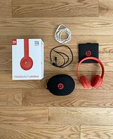 All items laid out on wooden floor, showing headphones, carrying case, two cables, user manual, and original box.