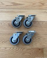 Four 4-inch industrial swivel casters with grey rubber wheels arranged on a wooden surface.