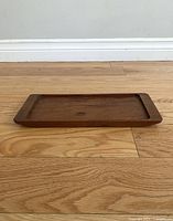 Rectangular Danish teak wood tray shown from side profile on wooden floor, displaying thickness and edge shape.