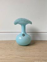 Front angle view of light blue handmade glass vase with ruffled pinched top edge, showing intact original maker sticker.
