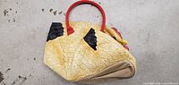 Left side angle shot of vintage style chicken shaped purse showing feather texture and red handle.