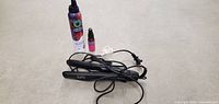Photo of black hair straightener on floor with cord, accompanied by Original Mineral Refresh Detox Treatment can and a small spray bottle with pink liquid