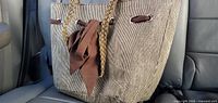 Large gold basket style tote beach bag sitting on a car seat showing its textured fabric and brown braided handles