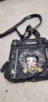 Black Betty Boop small handbag with Betty Boop graphic, silver-tone studs, zipper, and adjustable strap.