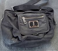 Juicy Couture black nylon crossbody bag showing front flap with silver zipper and brand plaque, adjustable shoulder strap visible, placed on carpeted surface.