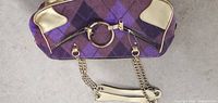 Close-up view of purple and brown plaid pattern bag with gold hardware and chain strap.