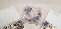 Three plastic jewelry organizer boxes, one with lid off showing assorted jewelry and accessories inside.