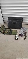 Full view of the computer briefcase bag with opened first aid kit, drill bit box, flashlight, hacky sacs, and ping pong balls on the ground.