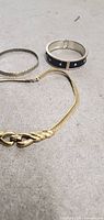 Gold tone necklace and three bracelets including silver cuff, thin twisted bangle, and medium-width bangle with black detailing.