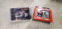 Two Harley Davidson metal tins, one opened and empty with motorcycle design, the other sealed unopened tin in original packaging with cards inside.