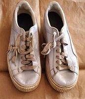 Top view of a pair of white Puma girls sneakers showing some wear and soiled laces.