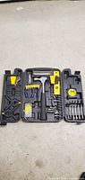 Open black plastic toolbox showing organized hand tools inside including hammer, pliers, tape measure, hex keys, clamps, screwdriver bits, and level.