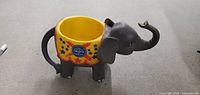 Photo of a ceramic cup shaped like a gray circus elephant with a yellow cup interior and circus tent graphics on the body.