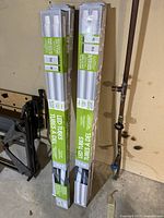 Two unopened boxes of LED tube replacement lights standing upright near a wall with pipes.