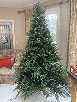 Full view of 7-foot artificial Christmas tree with dense green foliage set in a living room space, noted for minor wear and pre-lit capability though lights are not operating.