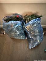 Two large blue plastic bags filled with synthetic Christmas garland.