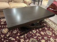 Overview of black rectangular coffee table in indoor setting on patterned rug showing top and part of surrounding furniture