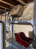 Side view showing wicker basket sled with black metal runners and two metal sled frames behind it on a storage shelf.