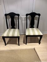 Front view of two black painted wooden dining chairs with striped beige and light green cushions.