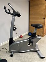 Side view of silver and black upright exercise bike showing seat, pedals, and base frame.