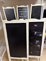Front view of three smaller chalkboards on top and two large chalkboards below, all with cream frames and black chalkboard surfaces, showing chalk writing and marks.