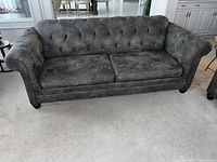 Full front view of gray Chesterfield sofa showing tufted back and seat cushions, rolled arms, and wood feet.