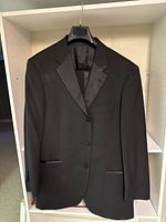 Black Hugo Boss suit jacket hanging on a hanger, showing the front with three buttons and satin lapel details.