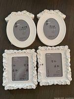 Top view showing all 4 white ornate IKEA KVILL picture frames, two oval and two rectangular, displayed on dark surface.