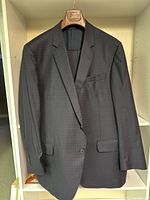 Front view of dark patterned men's suit jacket hanging on a wooden hanger.