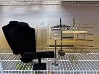 Shows black velvet necklace busts and T-bar bracelet stand alongside metal earring stands with multiple horizontal bars in black and gold metals.