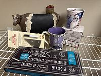 View of entire lot including cow statue, two ceramic mugs, and two sealed cheese marker sets