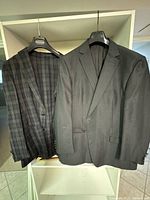Photo of two men's casual suit jackets hanging on a rack showing the overall look, one with a checkered pattern and the other with vertical pinstripes.