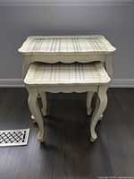 Stacked view of the two nesting side tables showing the plaid hand-painted tops and cream color with curved legs.