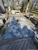Full view of the large blue floral outdoor rug laid out on wooden deck patio with outdoor furniture around