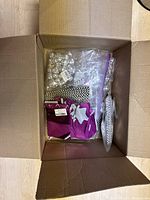 Open cardboard box showing party decorations including mini disco balls in plastic bags, black and white paper straws, and other packaged items.