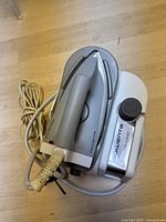 Photo of the Rowenta pressure iron on its base station showing the power cord and iron handle with Rowenta branding.