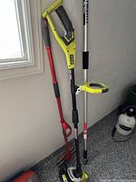 Photo of Ryobi weed whacker and red sponge mop leaning against wall next to a window