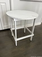 Side view of the white wooden side table showing round tabletop and straight legs with horizontal supports.