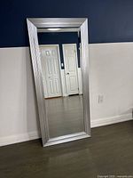 Full view of the silver framed full-length mirror leaning against a wall, showing its rectangular shape and modern silver textured frame.