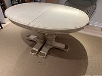 Side view of oval ivory painted solid wood dining table with pedestal legs.