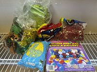 Various party decor items including latex balloons, balloon drop bag, Easter grass, and gold balloon weights on a shelf.