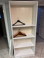 One white bookshelf assembled showing shelves inside and some hangers for scale
