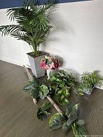 Overview of all faux plants and floral arrangements included in the lot showing the large tropical plant, pink hydrangea, small green plants in glass pots, and fiddle leaf fig branch.