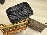 Three woven baskets, black lined basket on top, striped basket with handles underneath, and small brown basket beside them.