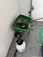 Photo showing Scotts Turf Builder with Edgeguard DLX push spreader with two wheels and part of green garden hose coiled nearby.