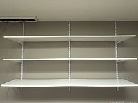 Front view of three white wall-mounted shelves installed on metal wall tracks.